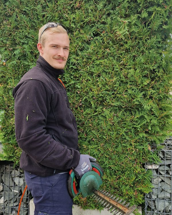 Jason Jattke vor einer geschnittenen Thujahecke